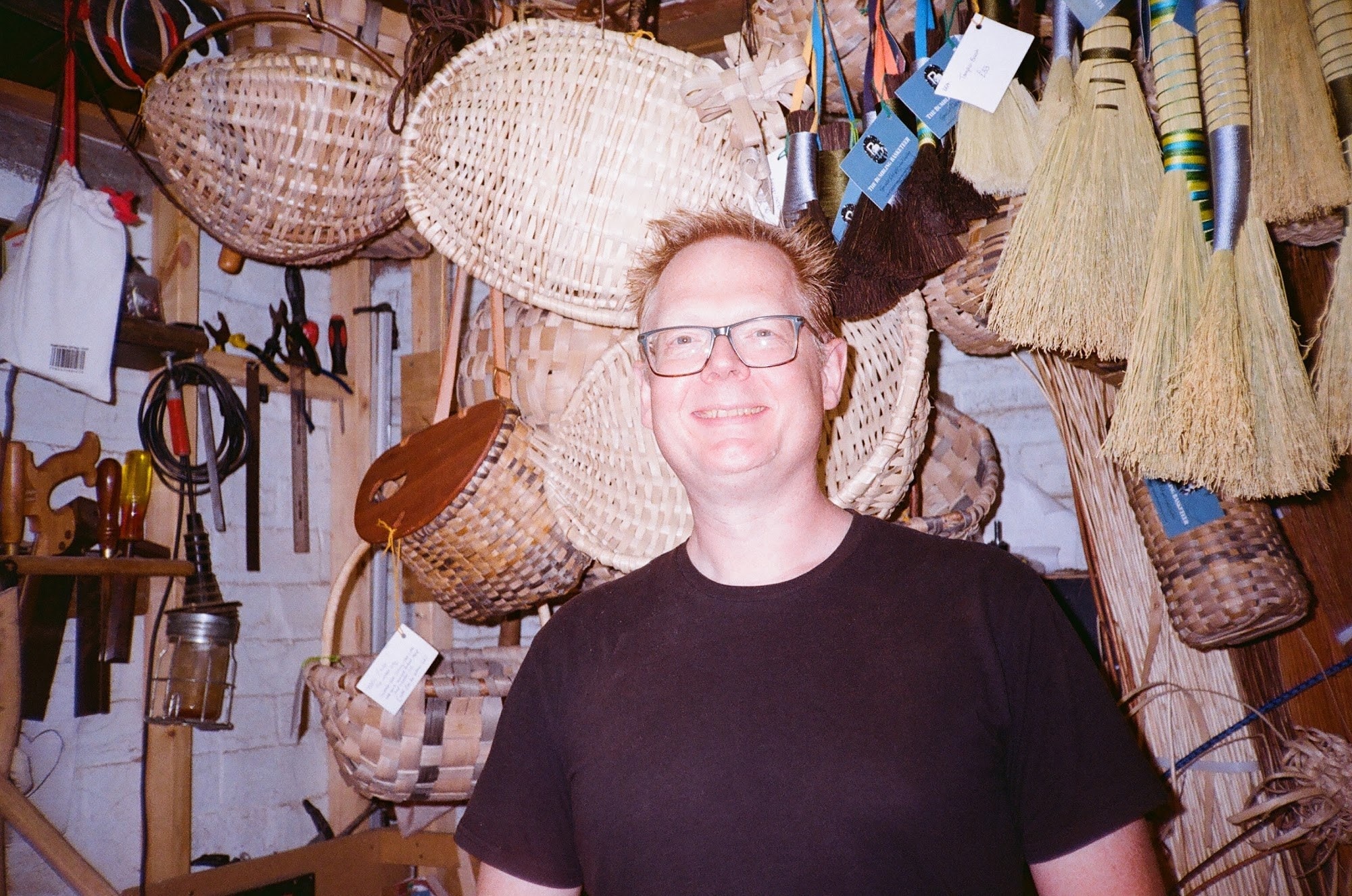 Simon Cooper in his workshop surrounded by hanging baskets, brooms and tools