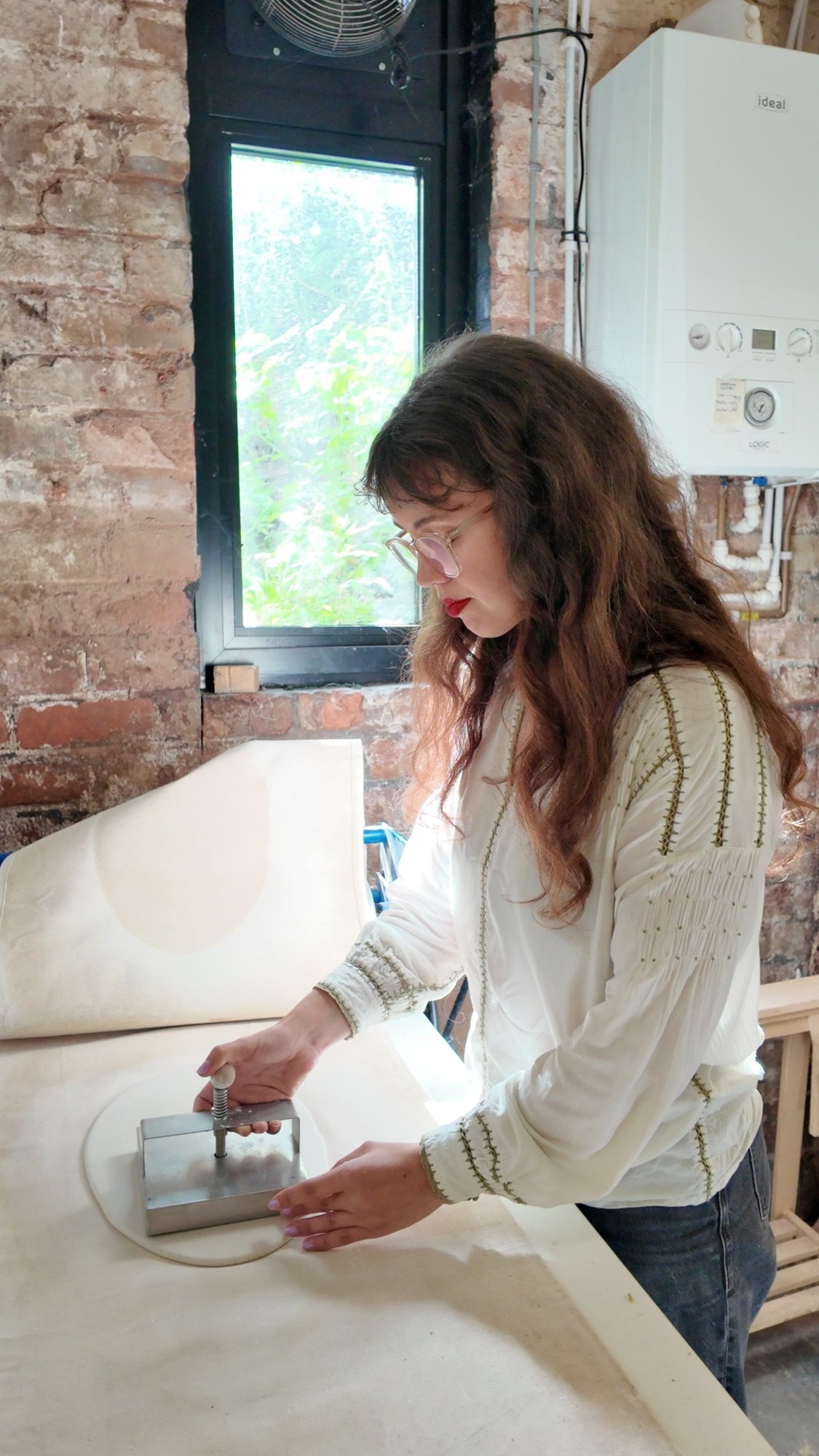 Bethan Hughes Jones pressing a metal cutter into a slab of clay at a workbench