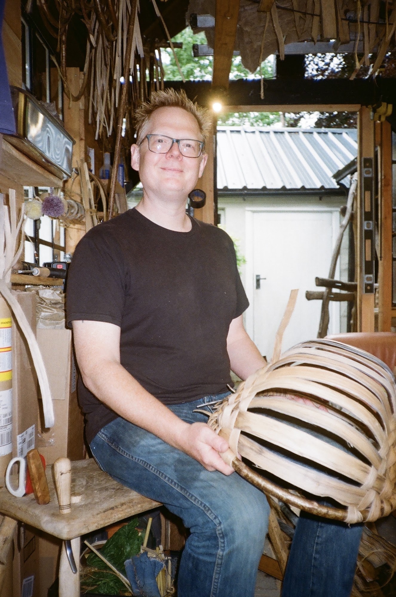 Simon Cooper seated in his workshop holding a half-woven swill basket
