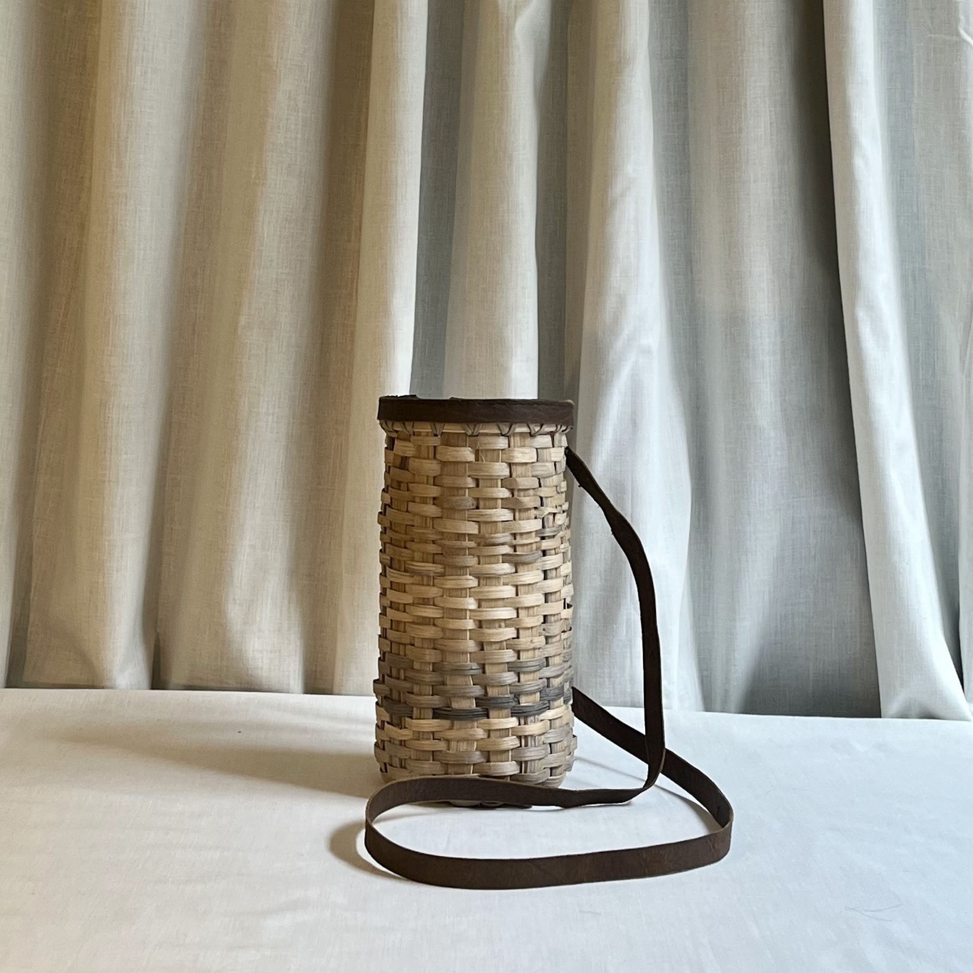 A tall oak bottle basket with a long dark leather strap