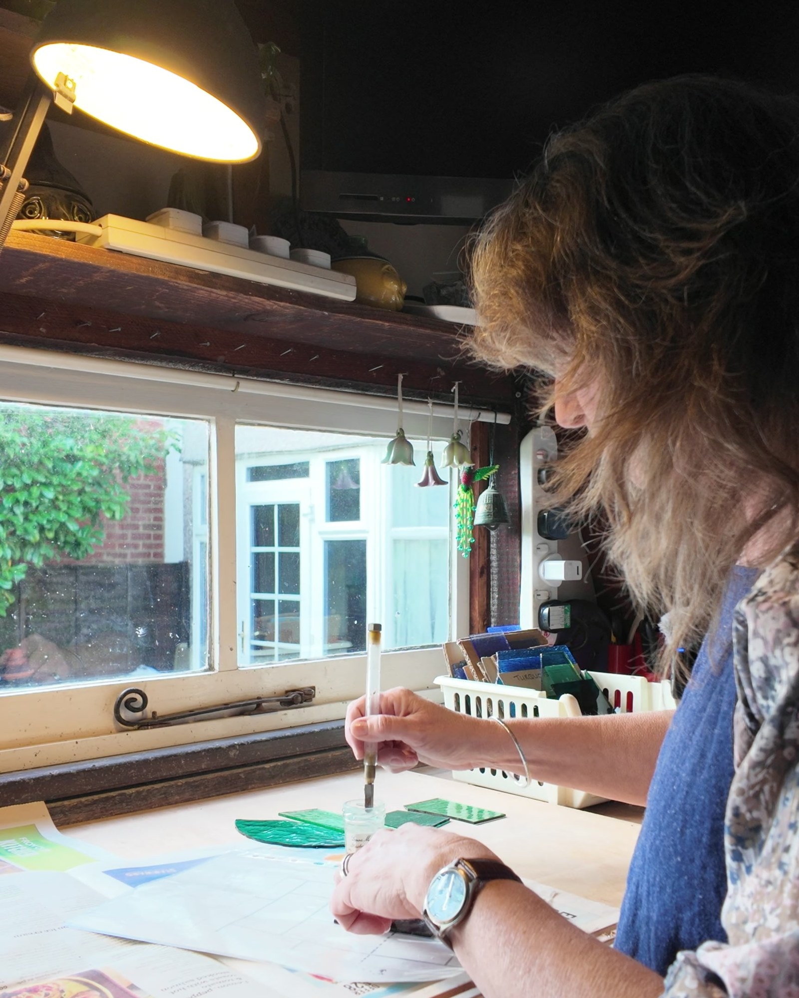 Mary Corkery at her workbench under the window, cutting a piece of green glass