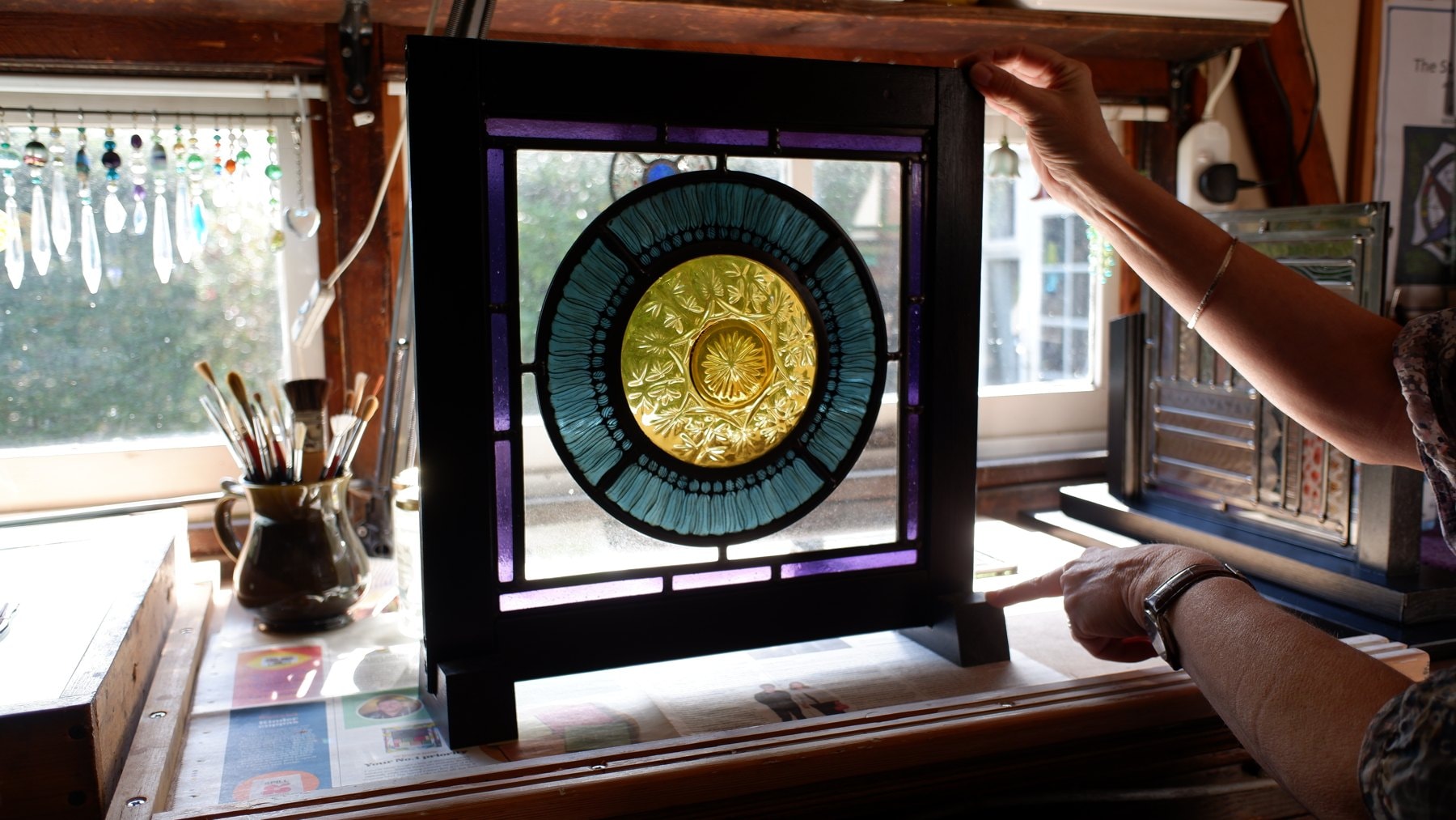 A leaded stained glass panel with a pressed-glass centre, standing in the workshop window