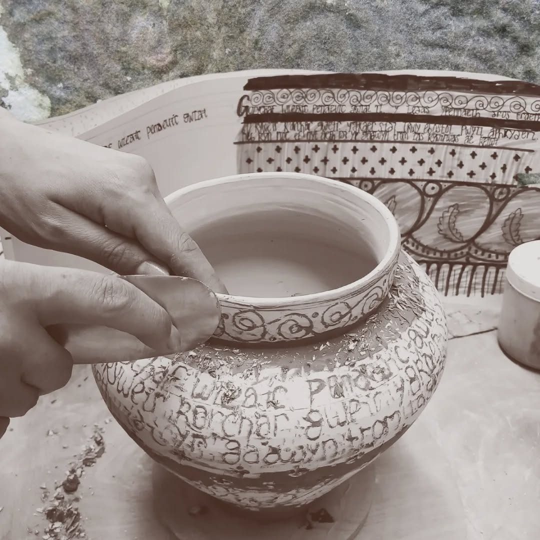 Hands scraping back slip on a ceramic pot covered in Welsh lettering