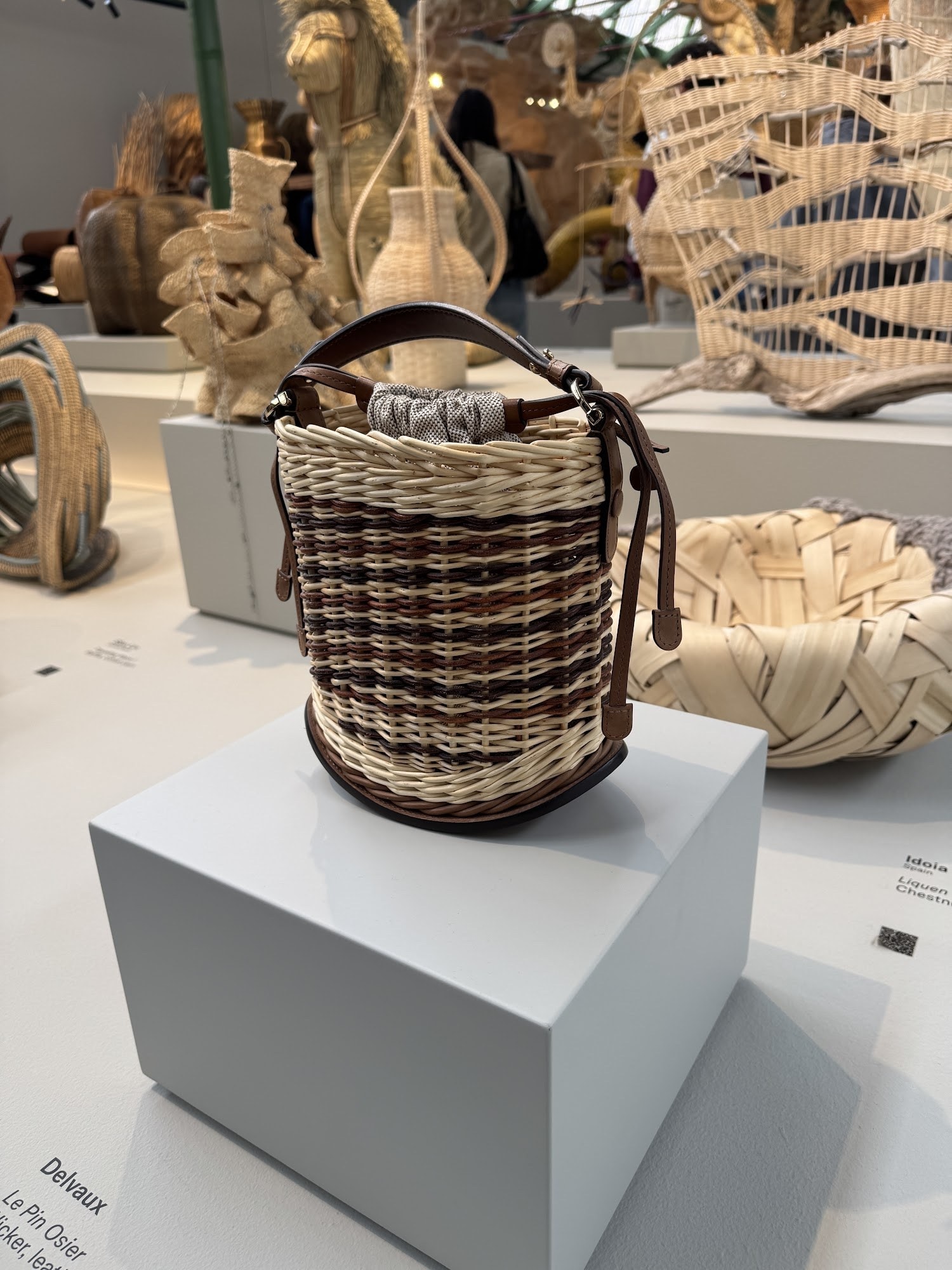 A wicker and leather basket bag displayed on a grey plinth