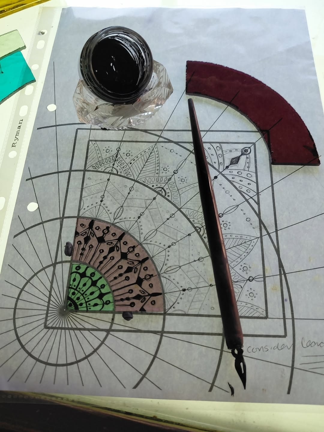 A dip pen and a pot of black glass paint on a paper cartoon beside a painted piece of glass