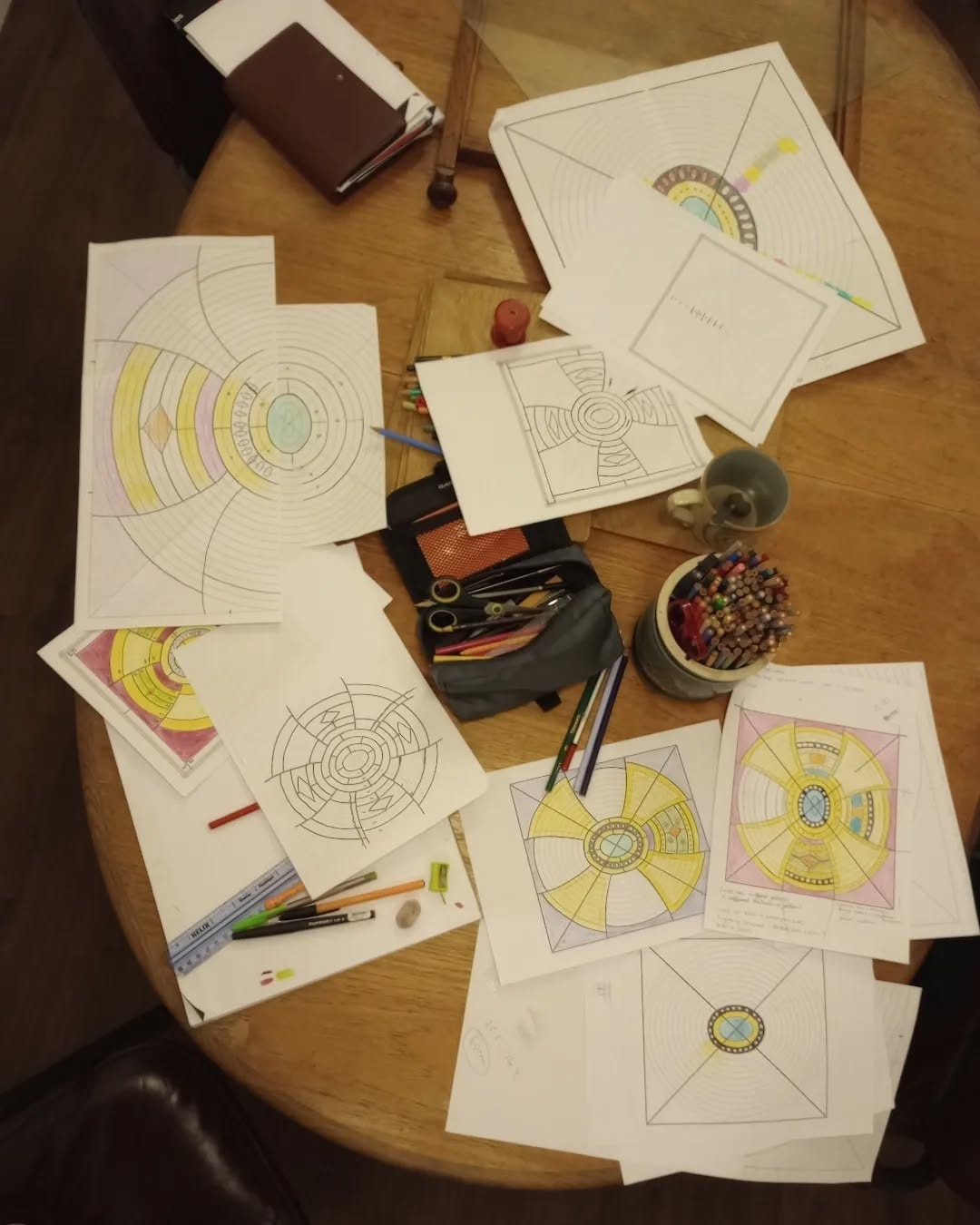Hand-drawn design cartoons for circular stained glass panels spread across a table with pencils and tools