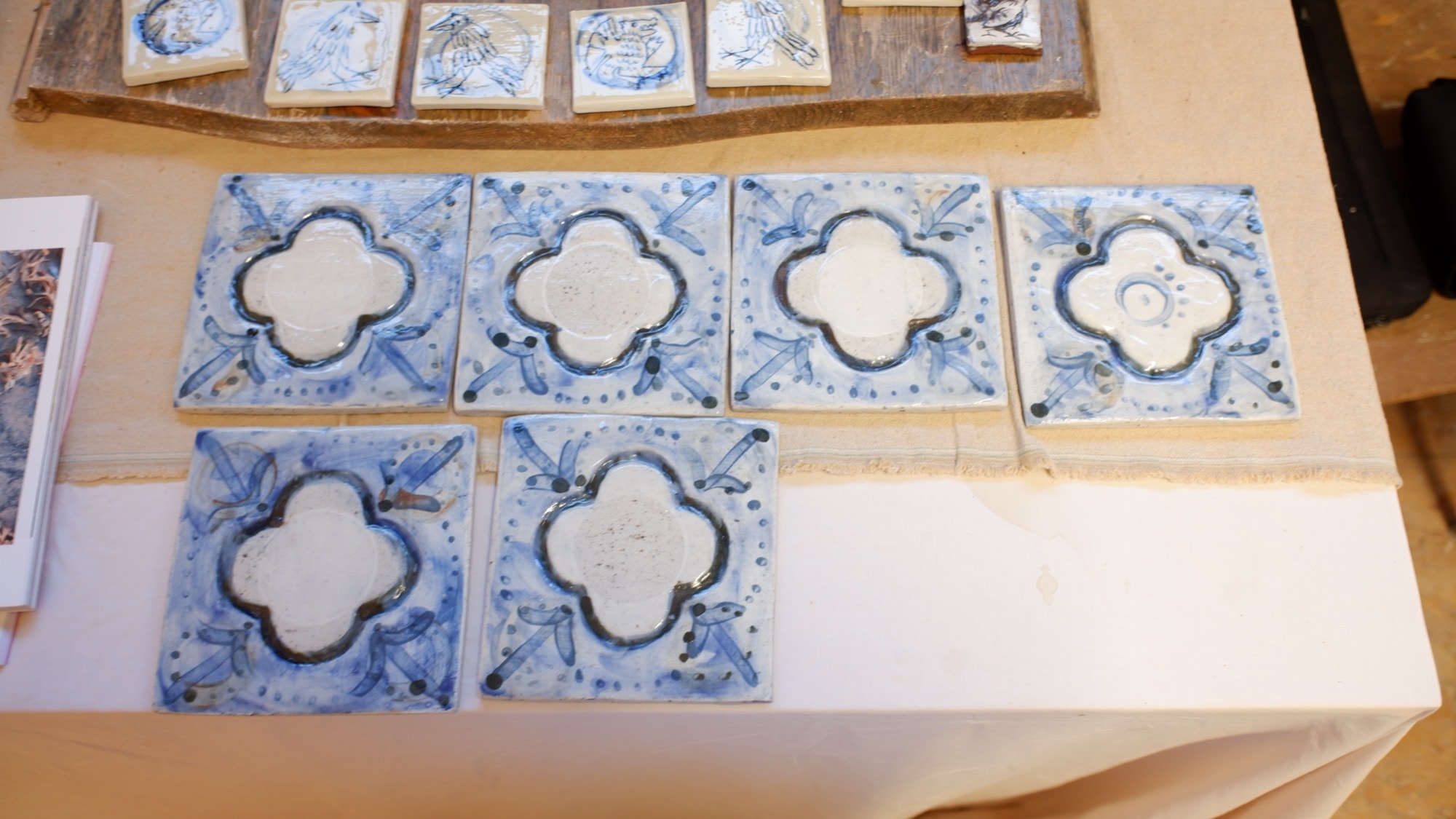 Six finished blue and white quatrefoil encaustic tiles laid out on a table