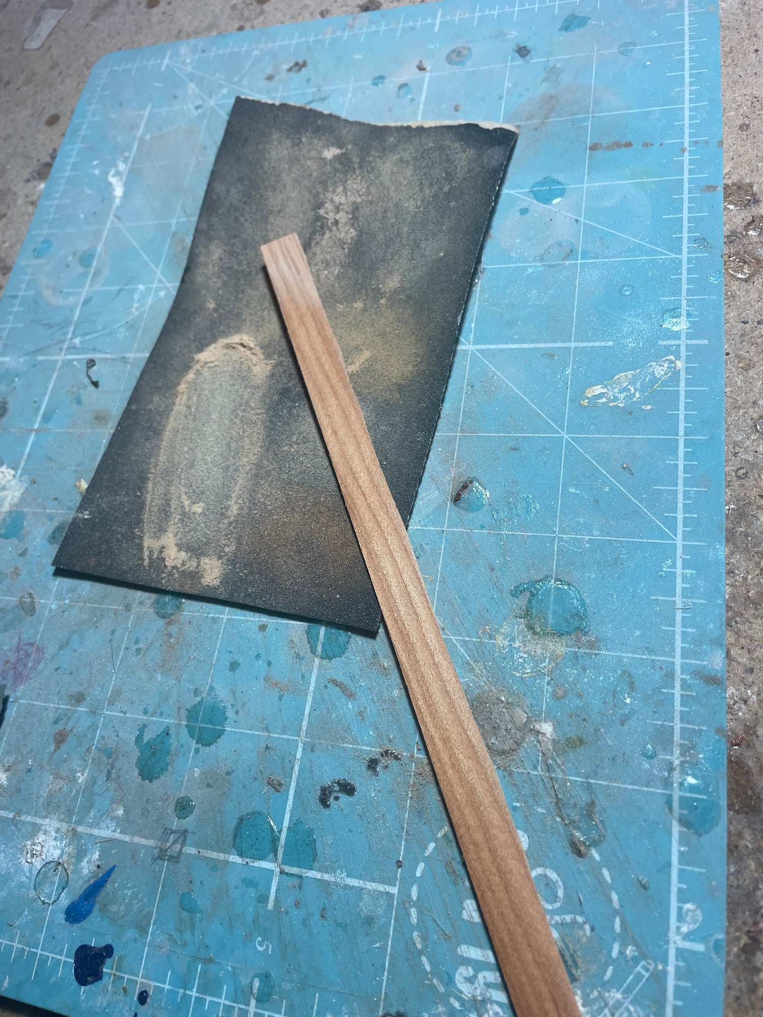 A thin strip of wood on sandpaper over a blue cutting mat