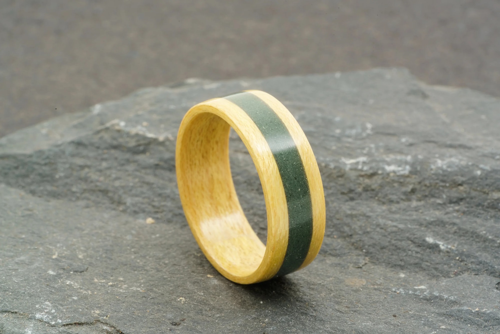 Pale maple bentwood ring with a dark slate inlay resting on a slab of slate