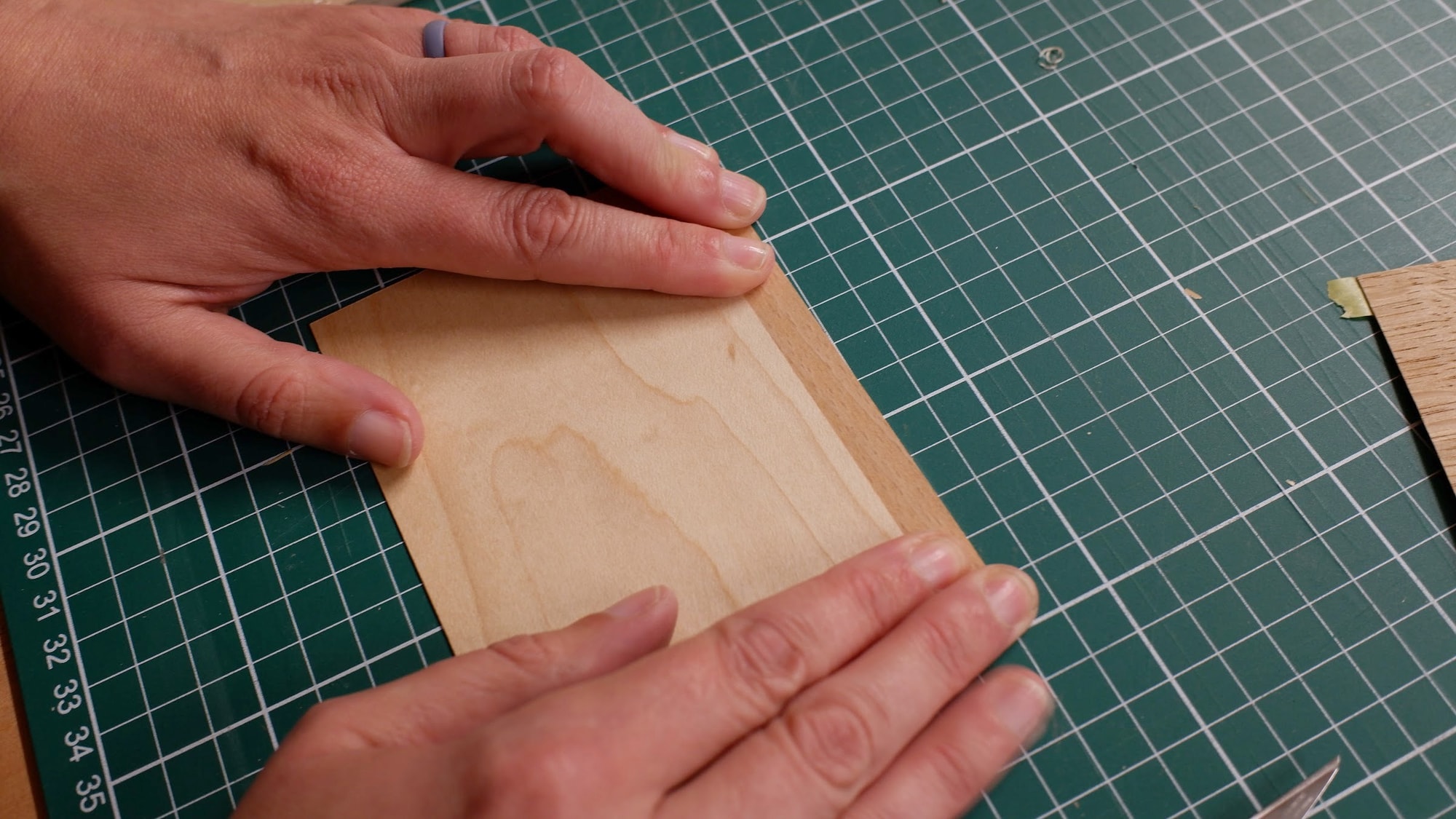 Claire Broad's hands pressing a cut oak veneer flat on a green cutting mat