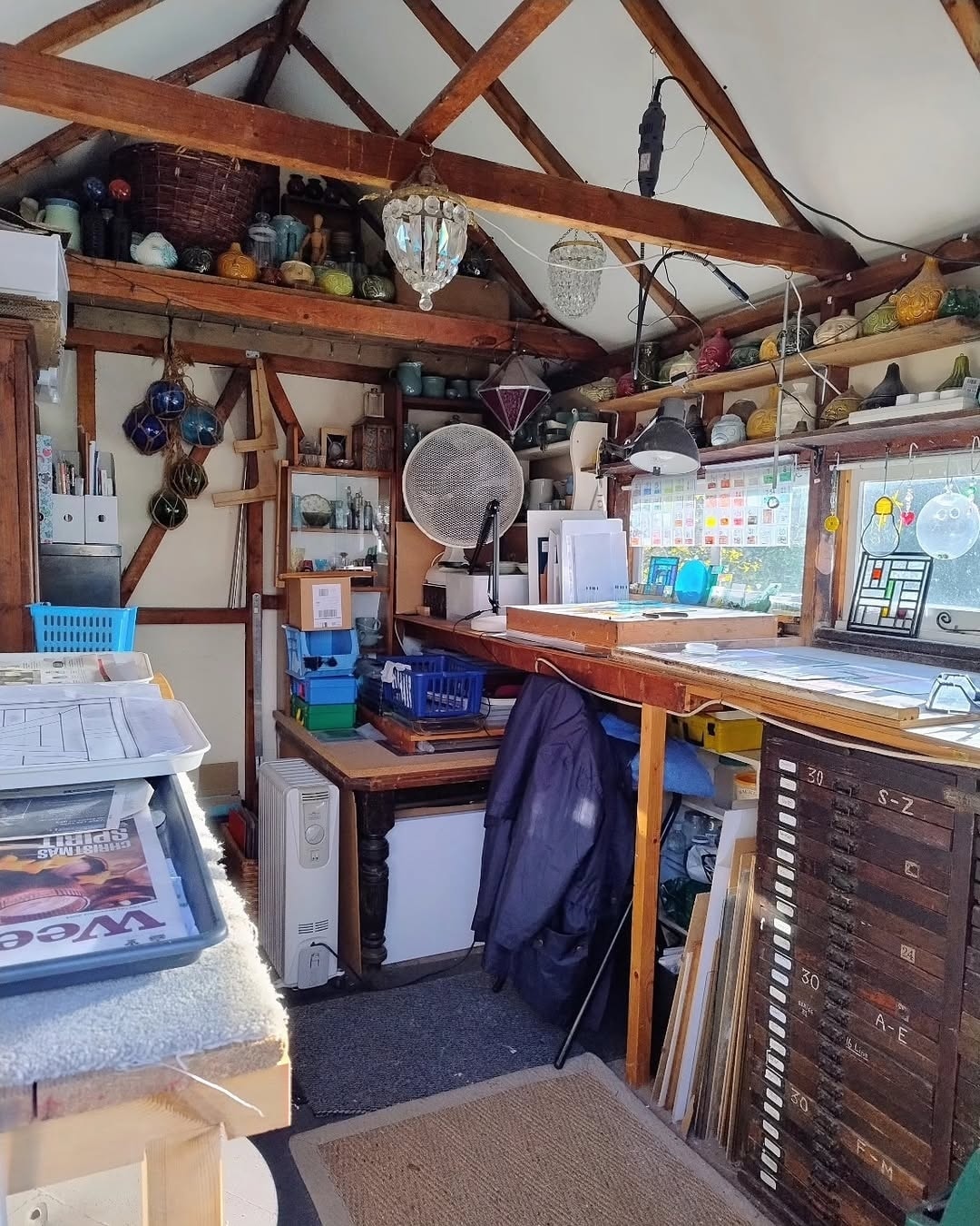 The inside of Mary Corkery's garden workshop, with open roof beams, workbenches and a plan chest of glass