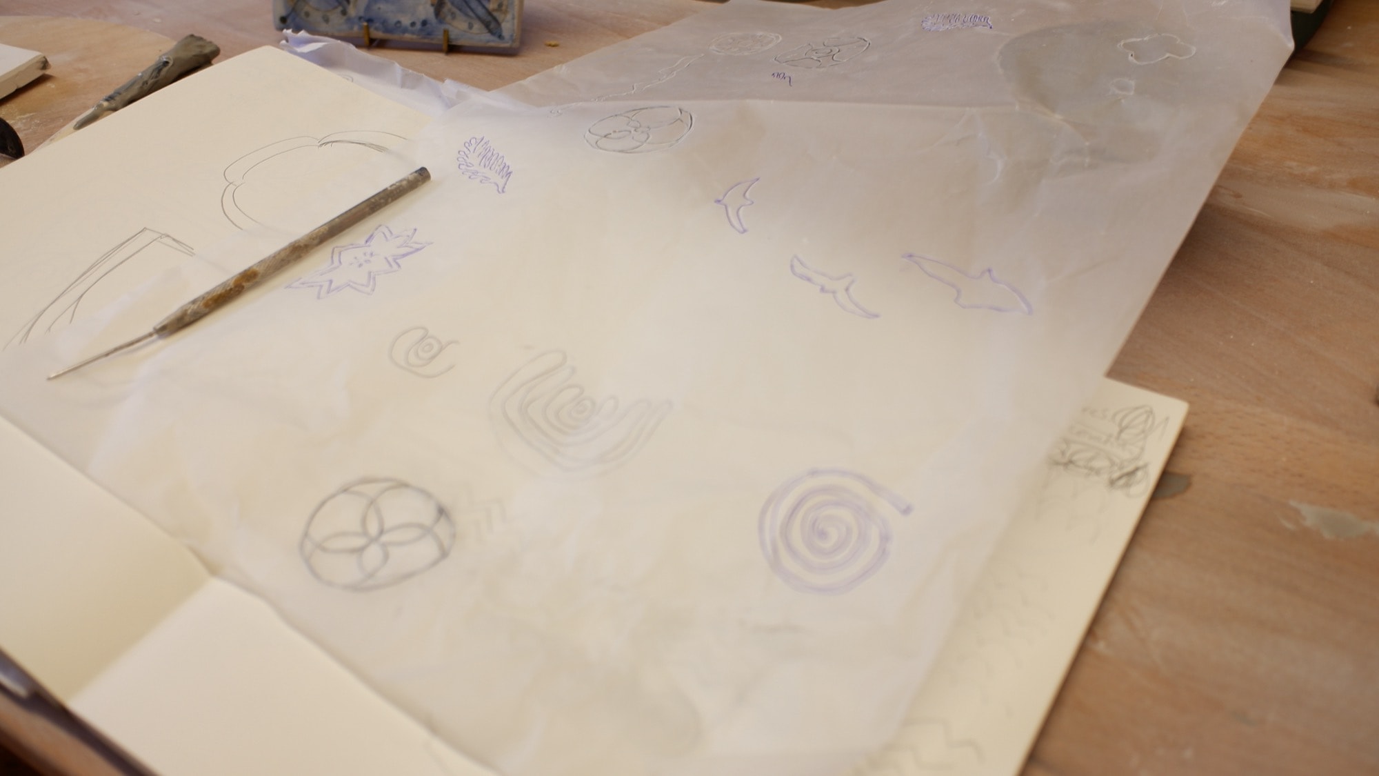 Pencil sketches of spirals, a quatrefoil and a four-petalled motif on tracing paper over a sketchbook
