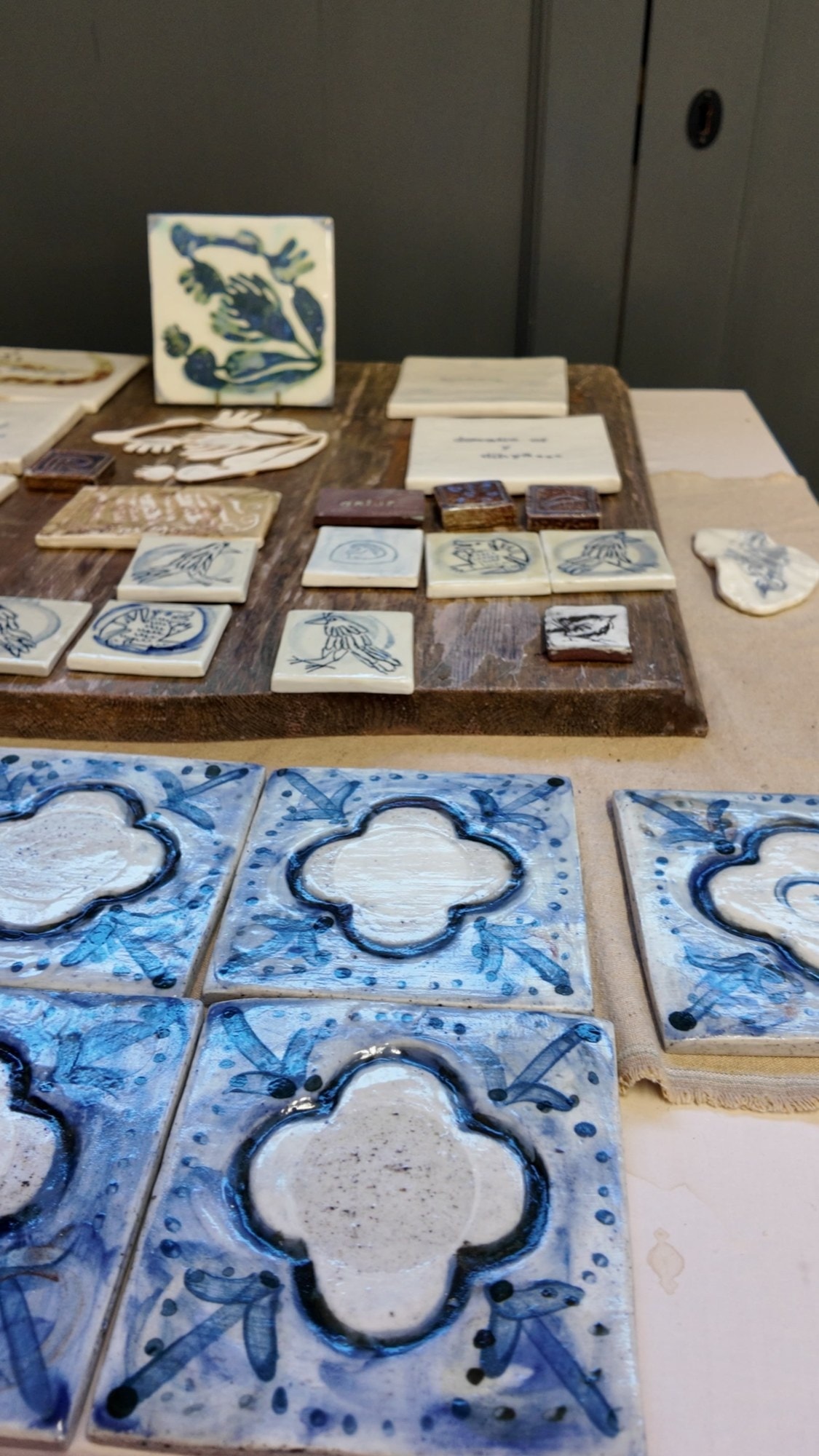 Blue and white quatrefoil tiles laid out on a table with smaller painted tiles behind