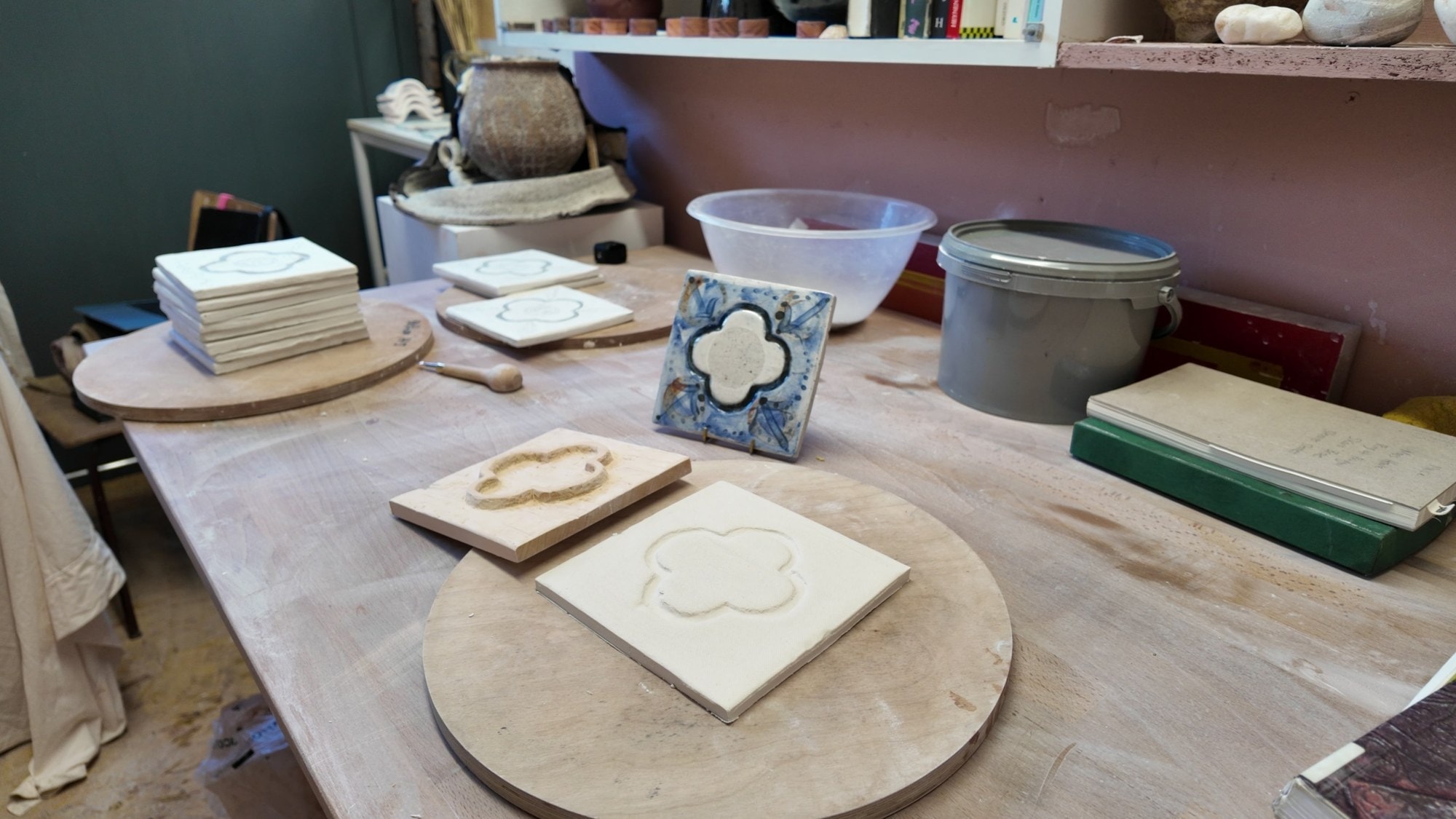 A pressed clay tile with a quatrefoil shape on a turntable, a finished blue tile behind