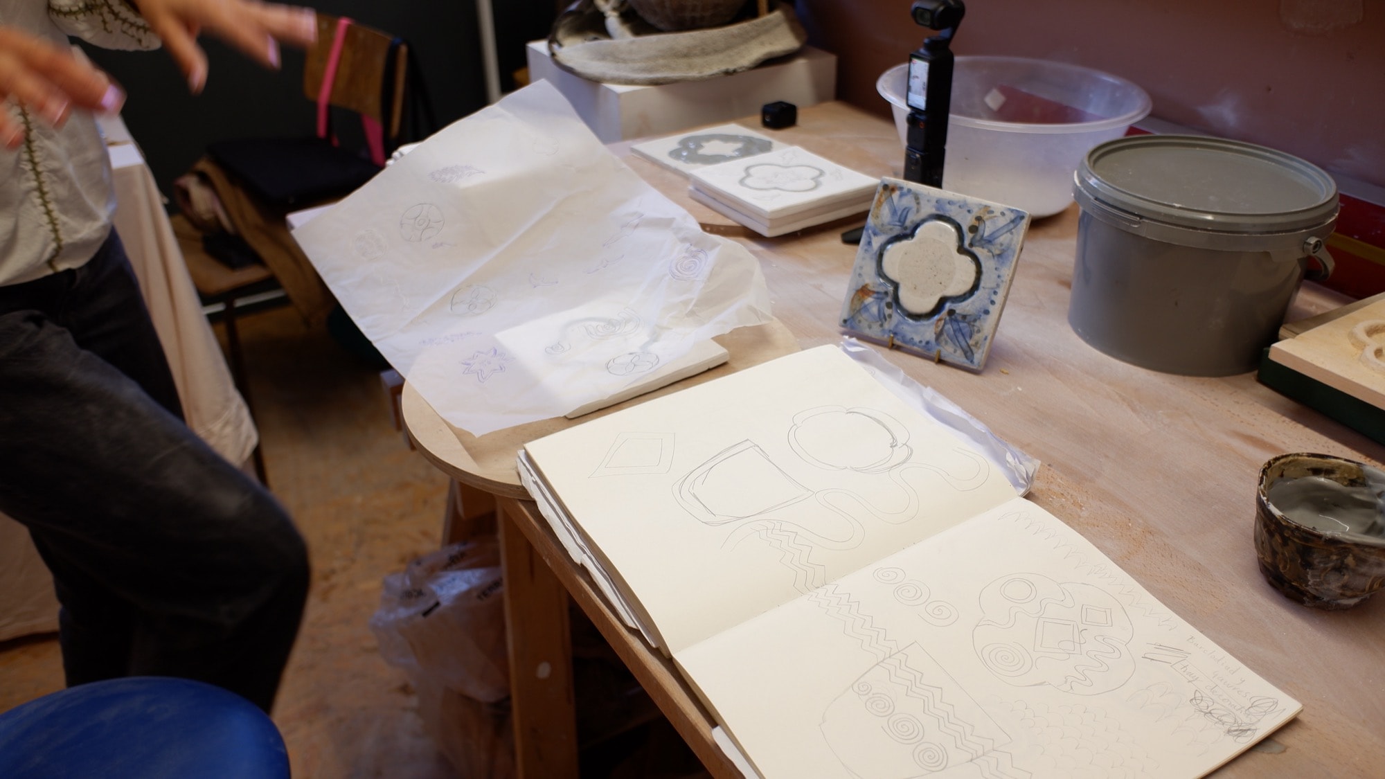 Bethan tracing a tile design from her sketchbook onto tissue paper at her table