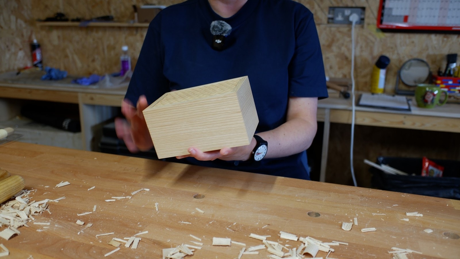 Claire Broad holding a pale carved wooden box across her workbench