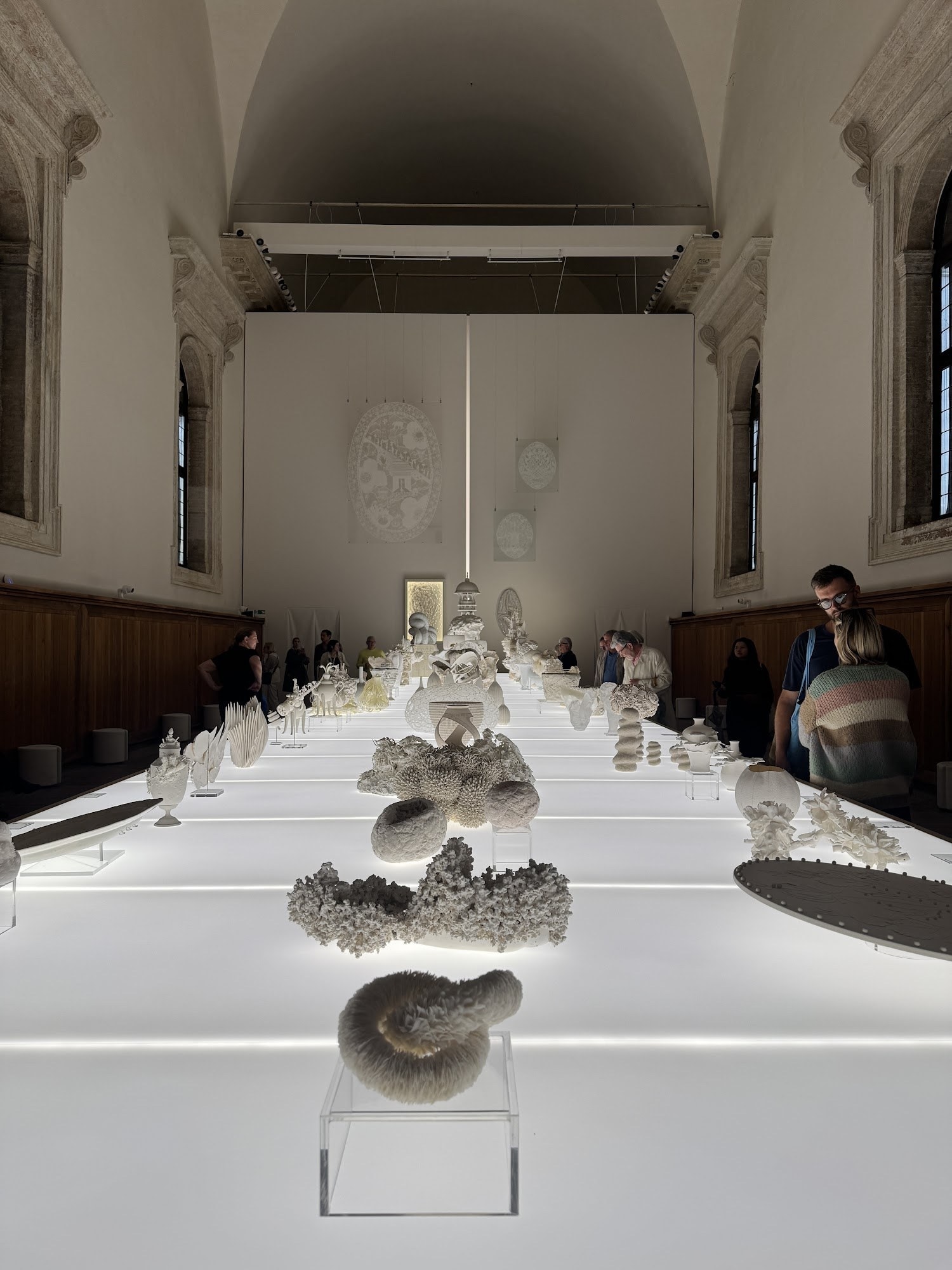 A long lit exhibition table lined with white ceramic pieces in a vaulted hall