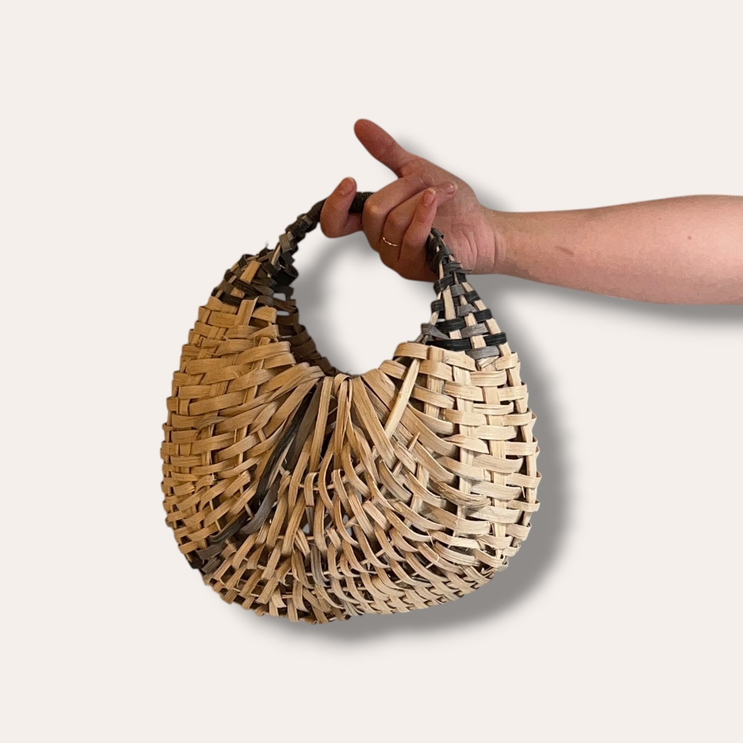 A hand holding a half-moon oak swill basket by its handle