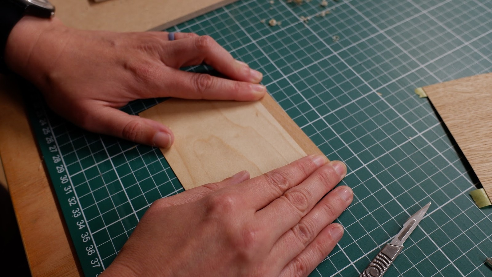 Two hands pressing a fitted veneer panel flat on a green cutting mat